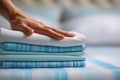 Person arranging a neatly folded stack of blue and white striped and solid fabric sheets on a bed with a cozy background setting Royalty Free Stock Photo
