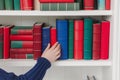 person arranging red, blue, green hardcover books on a white shelf