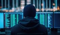 A person in a black hoodie focuses on multiple screens displaying code and data, symbolizing cybersecurity and hacking