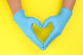 Person in blue latex gloves showing heart gesture against yellow background, closeup on hands Royalty Free Stock Photo