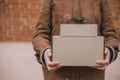 Person in brown coat holding simple paper carboard package