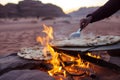 person cooking flatbread over an open fire in the desert Royalty Free Stock Photo