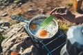 Person cooking fried eggs in nature camping outdoor, cooker prepare breakfast picnic on metal gas stove, tourism recreation Royalty Free Stock Photo