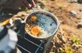 Person cooking fried eggs in nature camping outdoor, cooker prepare breakfast scrambled picnic on metal stove, tourism recreation Royalty Free Stock Photo