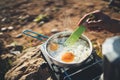 Person cooking fried eggs in nature camping outdoor, cooker prepare omelette breakfast picnic on metal gas stove, tourism recreat Royalty Free Stock Photo