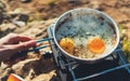 Person cooking fried eggs in nature camping outdoor, cooker prepare scrambled omelette breakfast picnic on metal stove, tourism Royalty Free Stock Photo