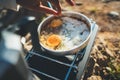 Person cooking fried omelette in nature camping outdoor, cooker prepare scrambled eggs breakfast picnic on metal stove, tourism Royalty Free Stock Photo