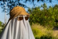 Person covered by a white sheet, with sunglasses and hat, in appearance of a ghost, in garden