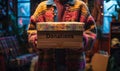 Person in a cozy sweater holding a cardboard box labeled Donations filled with clothing items to support charitable giving