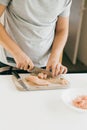 Person cutting chicken fillet with knife on wooden board on modern white kitchen. Process of making home pizza, hands close up. Royalty Free Stock Photo