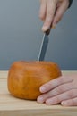 Person cutting with knife a slice of cheese wheel