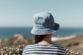 person with denim bucket hat, striped shirt, beachside