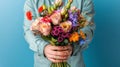 Person in denim shirt holding a vibrant bouquet of mixed flowers against a blue background. Royalty Free Stock Photo