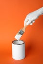 Person dipping brush into can of white paint on orange