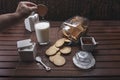 Person dipping a cookie into the glass of milk on a rustic wooden table