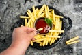 Person dipping French fries and tomato sauce