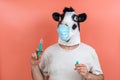 Person disguised as a latex cow mask wearing mask preparing injection for vaccination