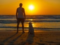 Person and dog watching together the sunset on the seashore.