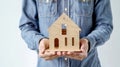 Person dressed in denim holds a small wooden house model, concept of home ownership Royalty Free Stock Photo