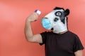 Person dressed in a latex cow mask wearing mask taking her temperature with an infrared thermometer