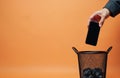 Person drops black mobile phone into trash bin. Hand discards old broken smartphone, creating electronic waste. Tech Royalty Free Stock Photo