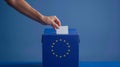 A person entering a vote into a ballot box European Union flag in background. European elections Royalty Free Stock Photo