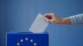 A person entering a vote into a ballot box European Union flag in background. European elections Royalty Free Stock Photo