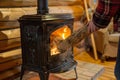 person feeding a log into a castiron stove in a log cabin interior