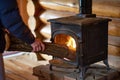 person feeding a log into a castiron stove in a log cabin interior