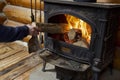 person feeding a log into a castiron stove in a log cabin interior