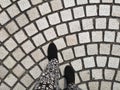 A person feet ware black shoes walking on grey cobblestone curve pattern paving on a street