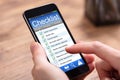 Person Filling Checklist Form On Cellphone At Wooden Desk