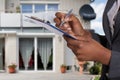Person Filling Document In Front Of House