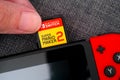 Person fingers inserting Super Mario Maker 2 video game cartridge into the Nintendo Switch video game console. Close-up