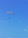 A person flying a orange paraglider in the blue sky.