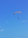 A person flying a orange paraglider in the blue sky.