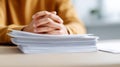 Close-up of hands resting on a large stack of papers on a desk with blurred background and person wearing a yellow sweater Royalty Free Stock Photo