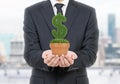 A person in formal suit holds a flowerpot with grass green dollar sign.