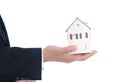 A person in formal wear holds a small house model in his hand