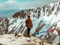 Person in a fur coat standing on the edge of a cliff and looking at Himalayas. Khardung La, India.