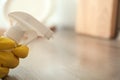 Person in gloves spraying detergent onto table indoors, closeup. Space for text