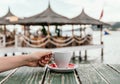 Person grabbing a cup of coffee on a wooden table at the beach Royalty Free Stock Photo