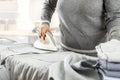 A person wearing a gray sweater ironing a shirt or a piece of gray fabric on an ironing board. Royalty Free Stock Photo