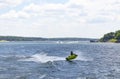 Person on a green PWC catches air on lake with other boats and PWCs and houses and docks on the shore in the background