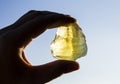 Person hand holding one yellow green lemon quartz crystal stone against sun and blue sky.