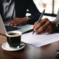 person hand holding a pen, signing a contract on desk with a laptop and coffee cup in the background Royalty Free Stock Photo