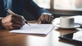 person hand holding a pen, signing a contract on desk with a laptop and coffee cup in the background Royalty Free Stock Photo