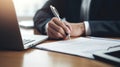 person hand holding a pen, signing a contract on desk with a laptop and coffee cup in the background Royalty Free Stock Photo