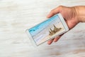 Person hand holding phone with photo of beach on wooden background Royalty Free Stock Photo