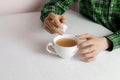 a person hand holding some sugar cubes and put them into cup of tea sitting at the table Royalty Free Stock Photo